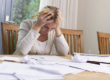 A woman sites a a table with all of her bills in front of her, frustrated with her hands on her head letting you know that Sttorney Lawyer Shane Zisman specializes in Corpoerate and personal bankruptcy filing and consulting.